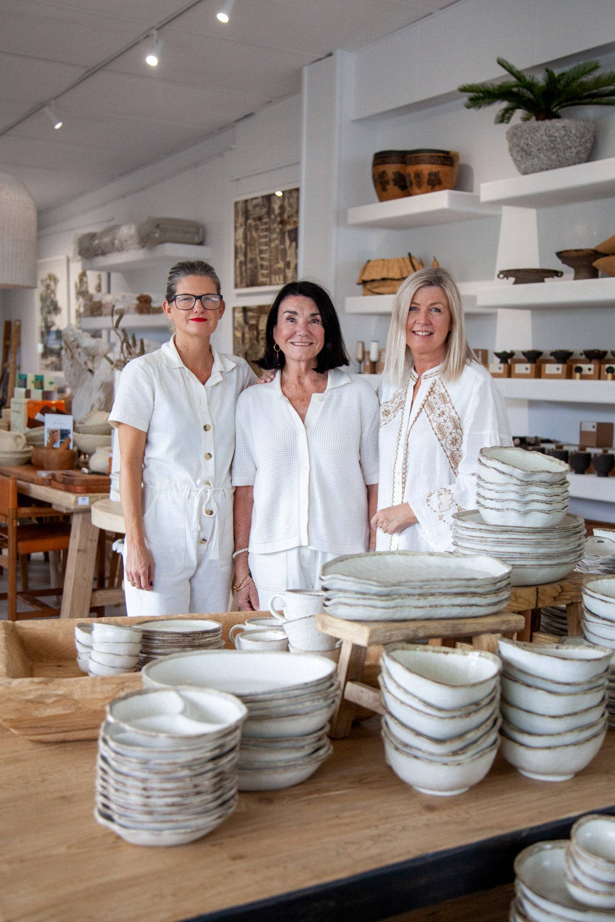 Three women standing behind a display of ceramic plates in a store.